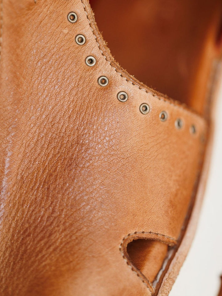 Close-up of The Tayten sandal by Savannah Sevens western life{&}style, featuring distressed leather, visible stitching, metal eyelets, and a textured surface with a partial white sole on the right.