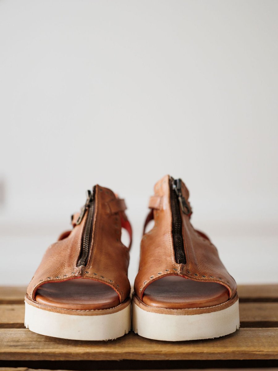 The Tayten sandals by Savannah Sevens western life{&}style, featuring brown statement zippers and white soles, are displayed side by side on a wooden surface against a plain background.