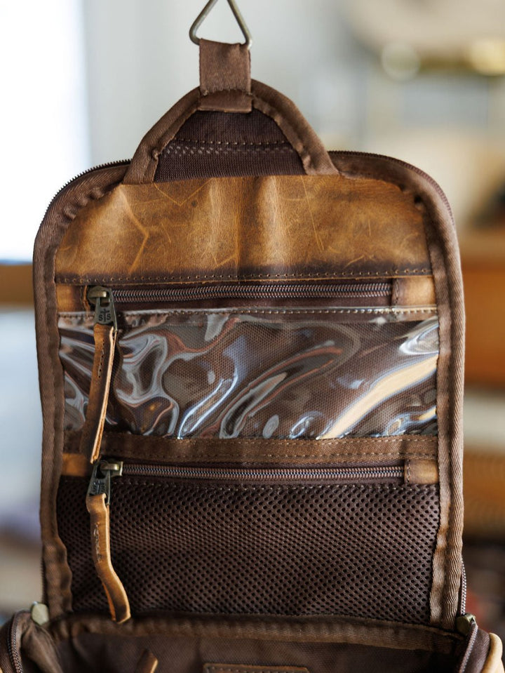 Close-up of the inside of The Toledo brown leather shave kit by Savannah Sevens western life{&}style, featuring transparent and mesh zippered compartments. This hanging toiletry bag is open, displaying its organized storage sections.