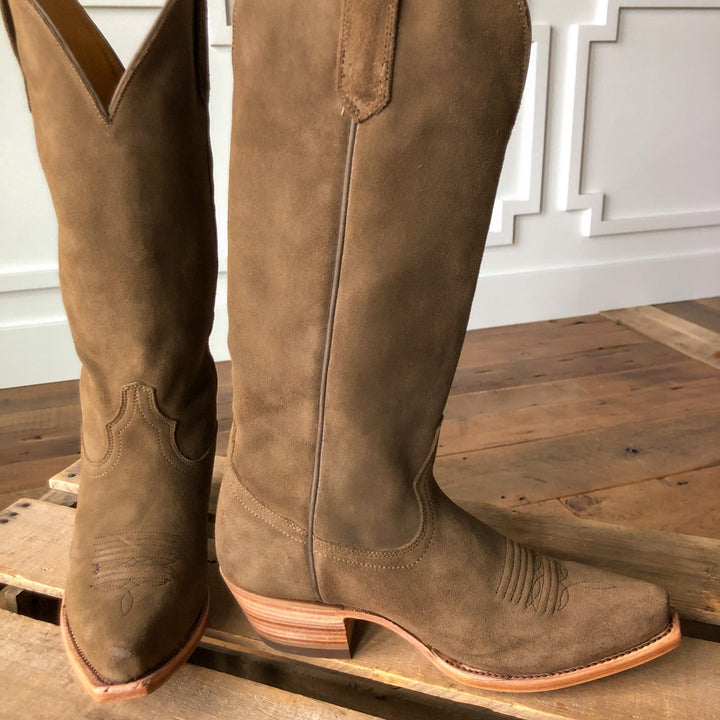 The Traver boots by Savannah Sevens western life{&}style, crafted from brown rough out leather with snip toes and wooden heels, rest on a wooden pallet floor before a white paneled wall.