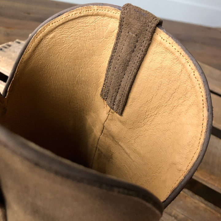 Close-up of the inside of The Traver boot by Savannah Sevens western life{&}style, featuring a pull tab, visible stitching, and smooth light brown leather lining, resting on a wooden surface.