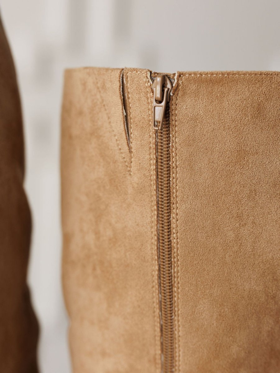 Close-up of The Tullos boot by Savannah Sevens western life{&}style, featuring tan faux suede, a round toe, and a visible side zipper. The soft texture is highlighted against a softly blurred background.
