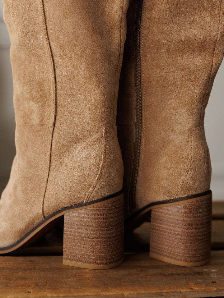 Close-up of The Tullos boots by Savannah Sevens western life{&}style—tan faux suede with chunky stacked wooden heels, round toes, and detailed stitching—standing on a wooden surface.
