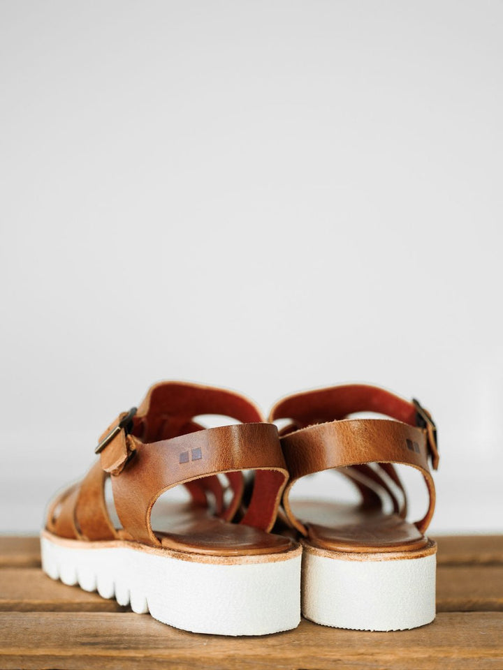 A pair of The Tuscola leather platform sandals by Savannah Sevens western life{&}style, featuring cushioned insoles and white chunky soles, sits on a wooden surface against a plain light background. Sandals made by BedStu.