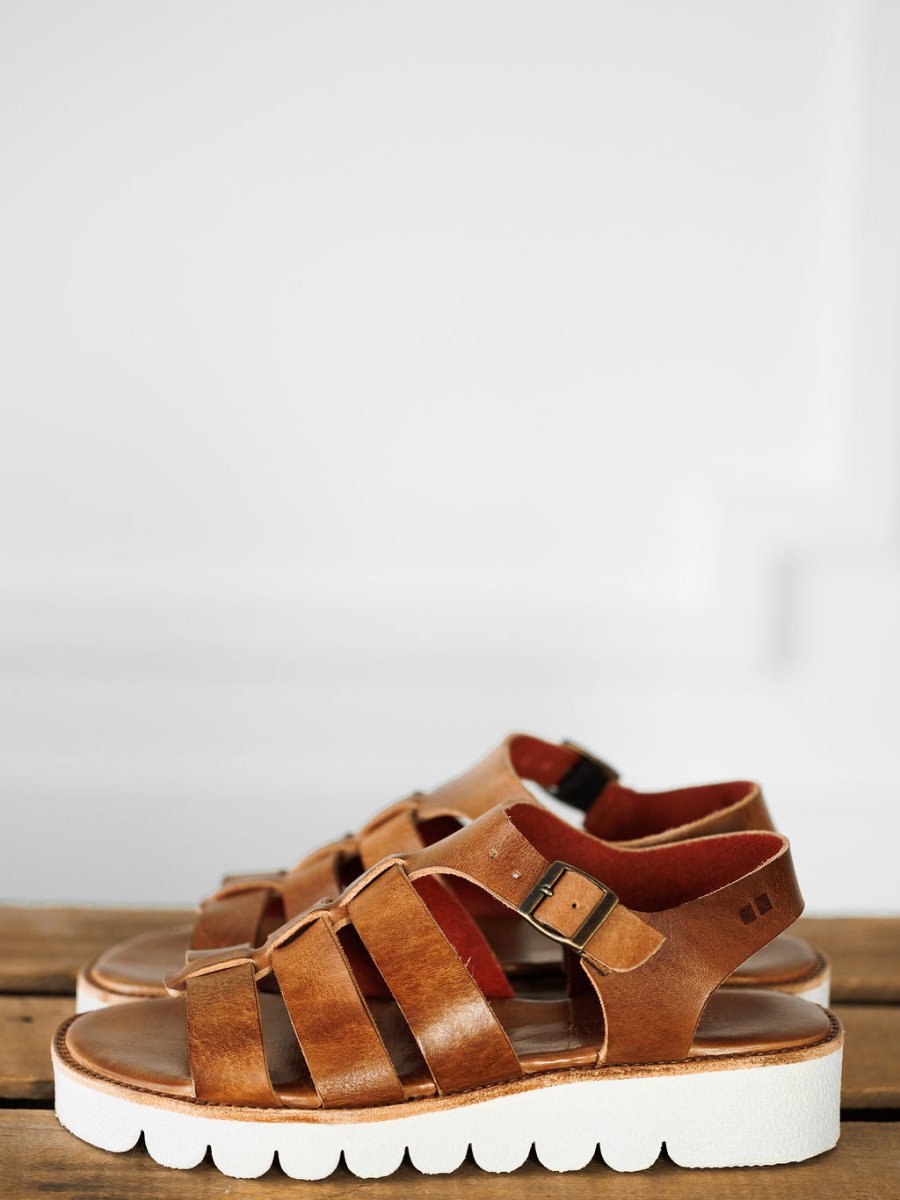 A pair of The Tuscola brown leather platform sandals by Savannah Sevens western life{&}style, featuring multiple straps, cushioned insoles, and white chunky soles, displayed side by side on a wooden surface against a light background.