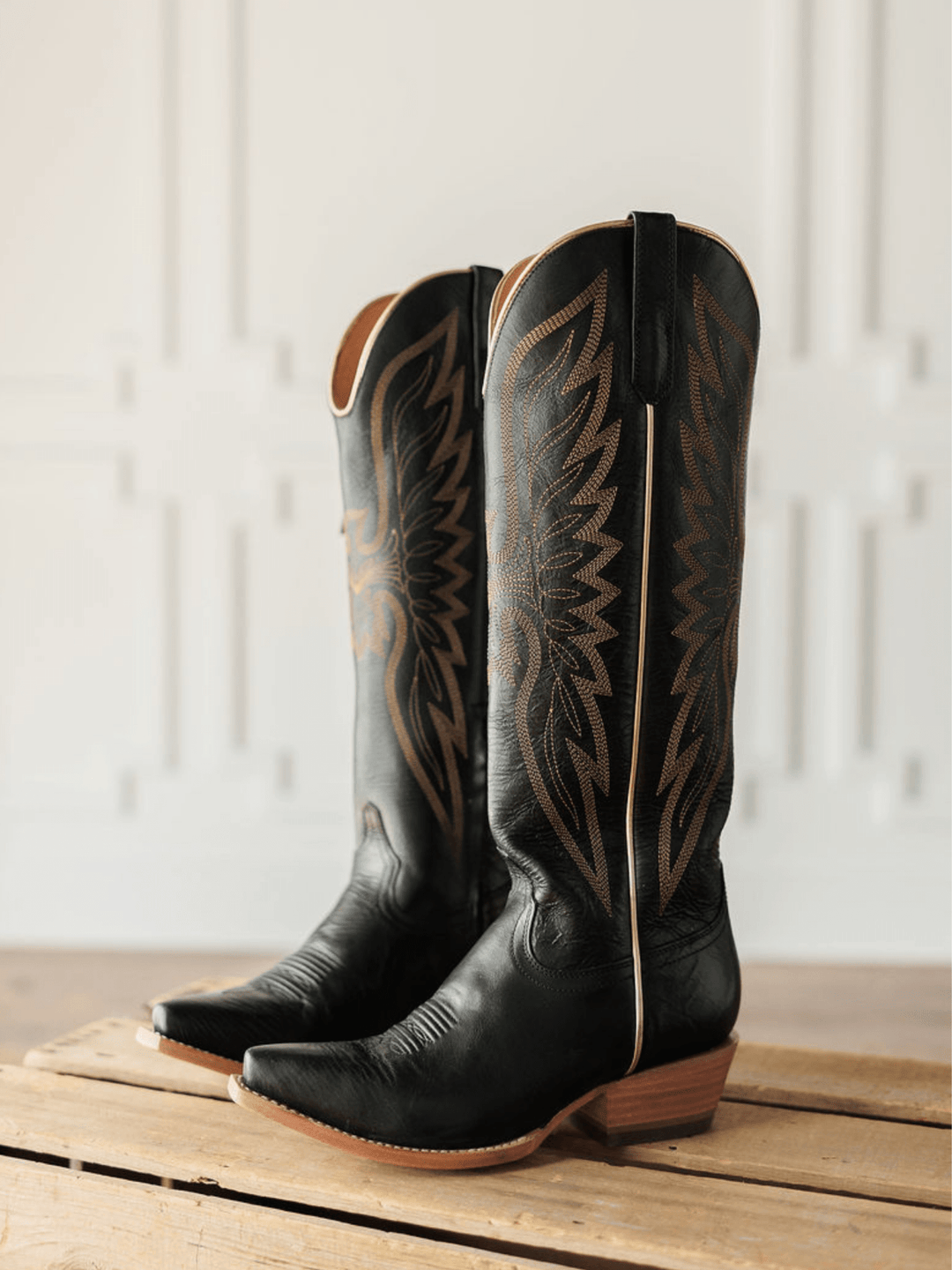 The Vaquera by Savannah Sevens western life{&}style—black leather snip toe boots with brown western embroidery—rest atop a wooden crate, set against a light, decorative backdrop. Made by Black Star. 
