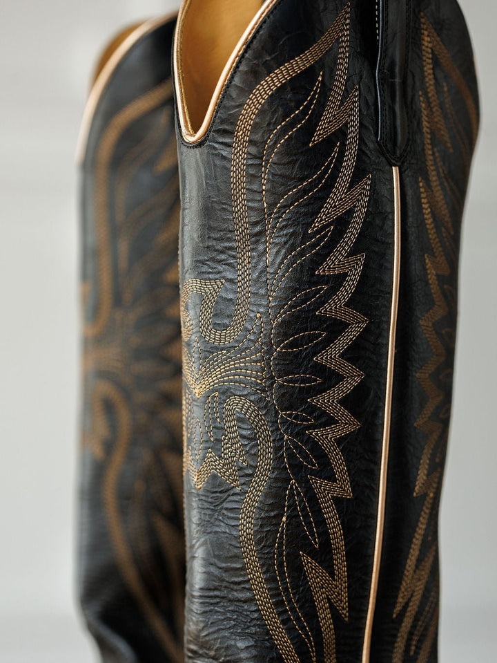 Close-up of The Vaquera boots by Savannah Sevens western life{&}style: black leather snip toe design with intricate golden western embroidery in a wing or flame pattern along the side. Made by Black Star. 