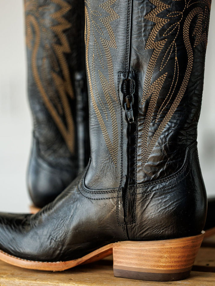 Close-up of The Vaquera black leather snip toe boots by Savannah Sevens western life{&}style, featuring brown western embroidery, wooden heels, detailed texture, and a side zipper. Made by Black Star. 