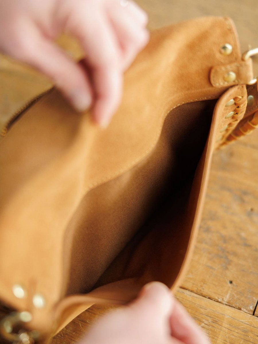 A close-up of hands holding open The Yoakum leather bum bag by Savannah Sevens western life{&}style, showing its empty fabric-lined interior with a single pocket and snaffle bit detail, resting on a wooden surface.