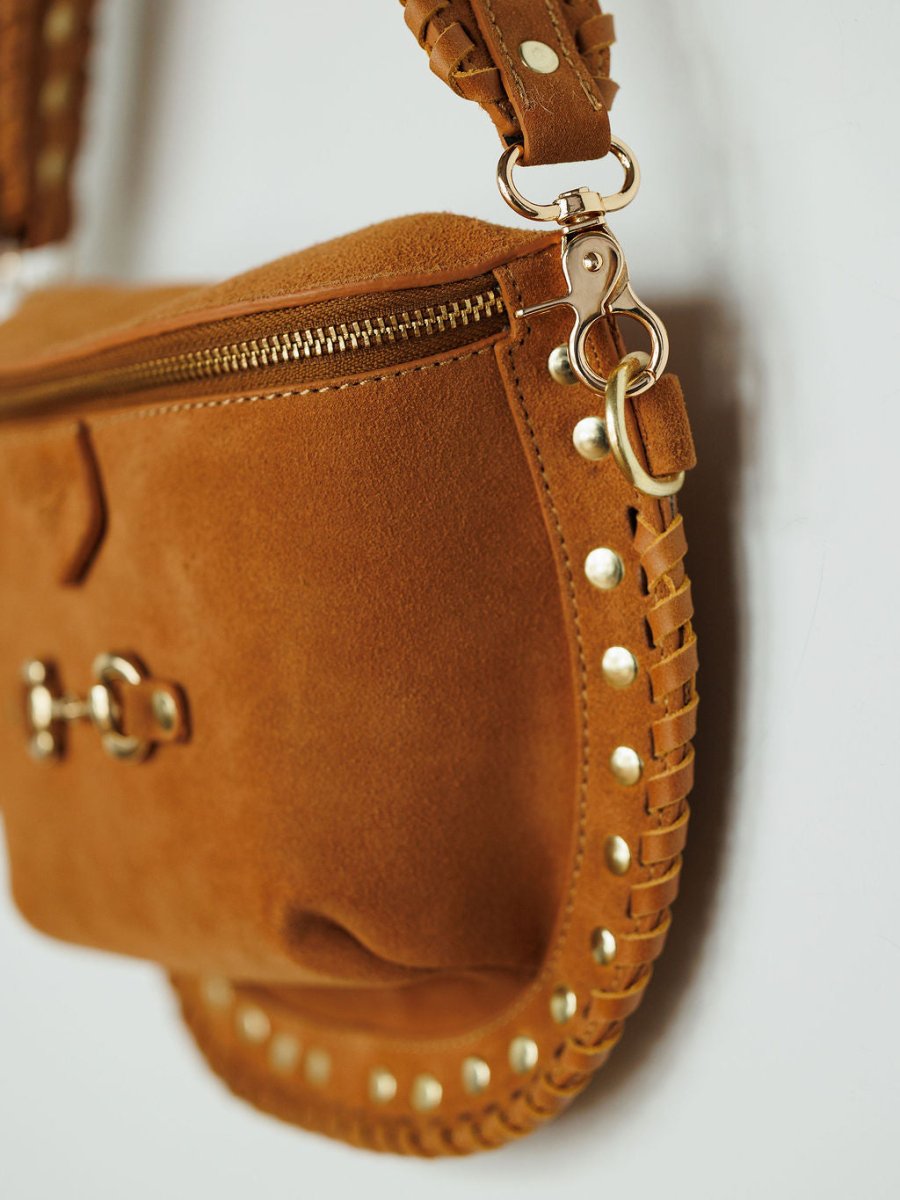 Close-up of The Yoakum by Savannah Sevens western life{&}style—a brown suede handbag with gold zipper, decorative gold studs, braided leather edge, and a detachable strap secured by a gold clasp for versatile style.