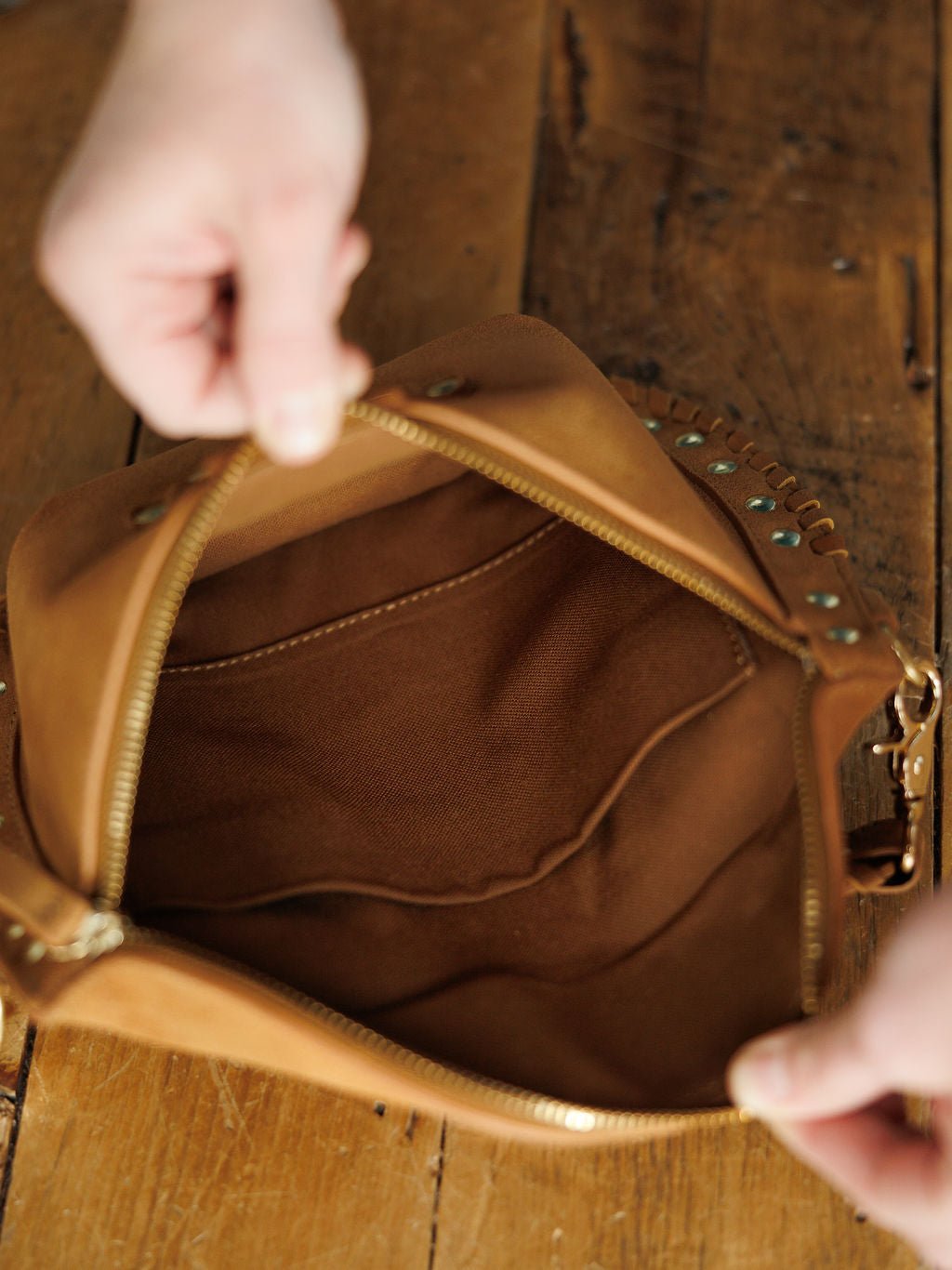A person holds open The Yoakum leather bum bag by Savannah Sevens western life{&}style, displaying its suede interior and inner pocket on a wooden surface.
