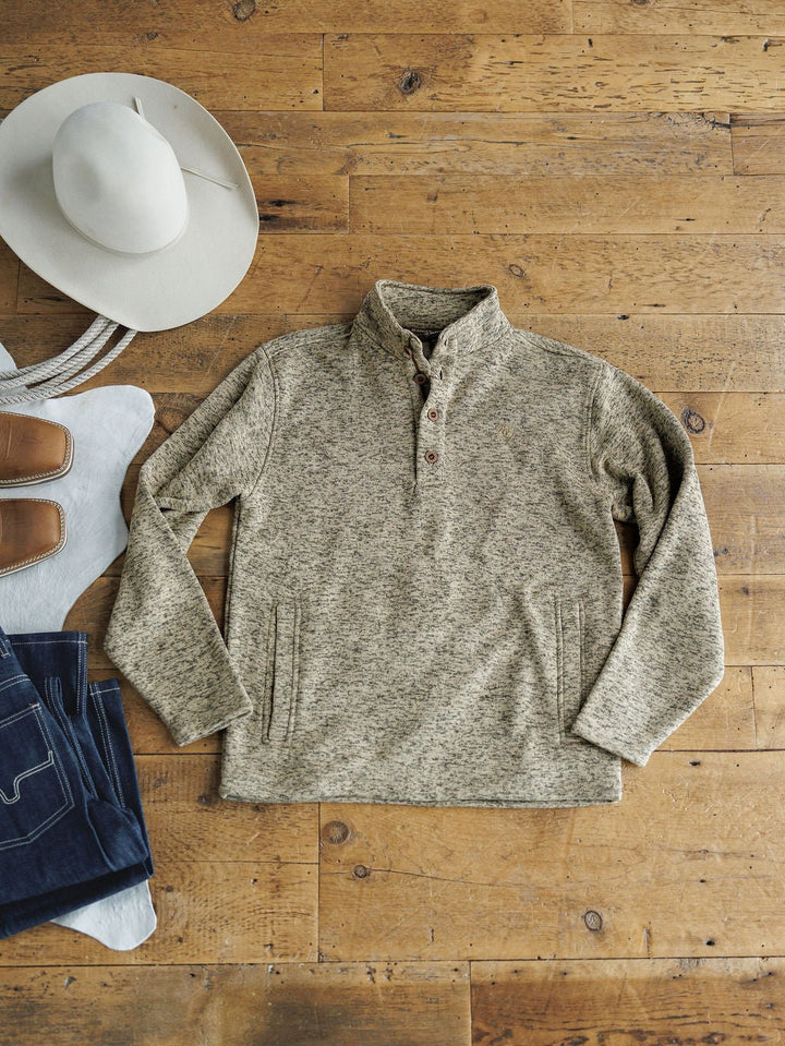 A Thompson Ariat Men's Pullover from Savannah Sevens western life{&}style, in beige, is displayed on a wooden floor beside a white cowboy hat, brown boots, rope, and dark jeans. This fleece-lined style ensures comfort and moisture-wicking performance.