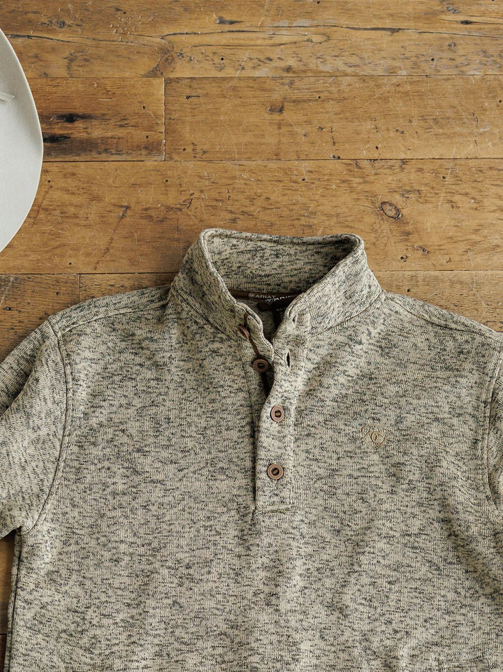 The Thompson Ariat Men's Pullover by Savannah Sevens western life{&}style, a heathered gray long-sleeve henley with a stand collar and three brown buttons, is laid flat on rustic wood. A white hat peeks in at the top left corner.