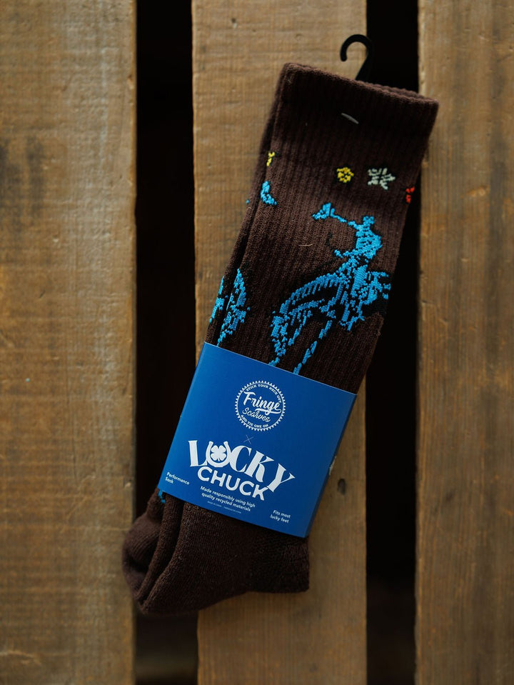 A pair of Tie One On Crew Socks by Savannah Sevens western life{&}style, featuring blue and yellow patterns, is shown with a "Lucky Chuck" label on a rustic wooden surface.