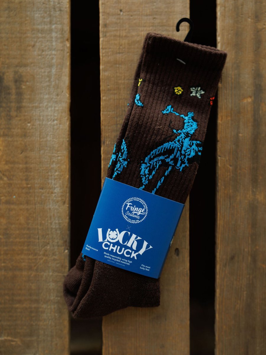 A pair of Tie One On Crew Socks by Savannah Sevens western life{&}style, featuring blue and yellow patterns, is shown with a "Lucky Chuck" label on a rustic wooden surface.