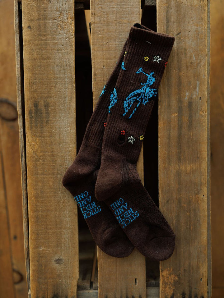 The Tie One On Crew Socks from Savannah Sevens western life{&}style are brown, odor-fighting hemp blend crew socks with blue embroidery and colorful stitching. Blue “Stock Tank Animal Only” text decorates the soles.