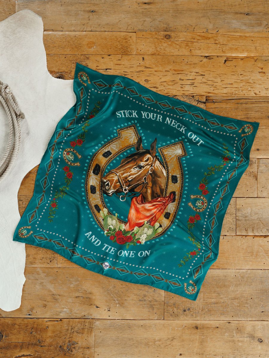 The Tie One On Neck Scarf by Savannah Sevens western life{&}style displays a western show horse head in a gold horseshoe with roses and greenery on teal, plus the phrase "Stick your neck out and tie one on," styled on wood flooring near a white rug.