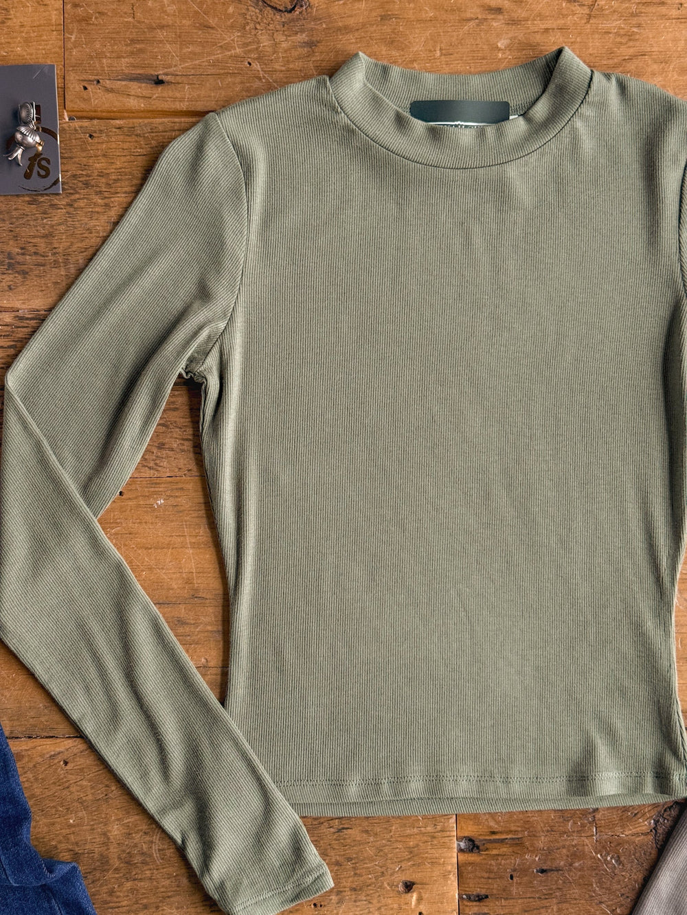 The Tifton Silver Sage Ribbed Basic Top by Savannah Sevens western life{&}style, a long-sleeve ribbed style in a subtle silver sage tone, is displayed lying flat on a wooden surface. 