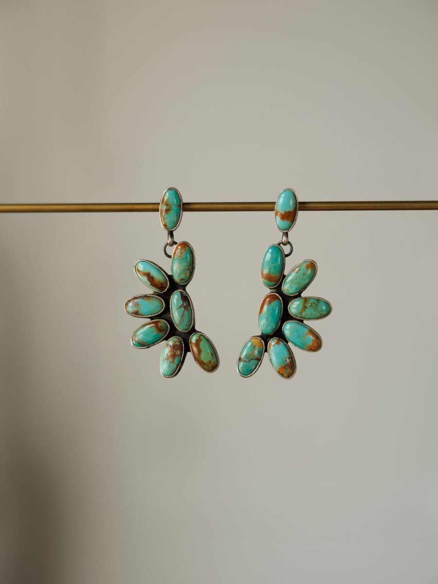 The Tijeras Earrings by Savannah Sevens western life{&}style feature dangling sterling silver with clusters of oval Kingman turquoise in a fan pattern, showcased on a plain beige background.