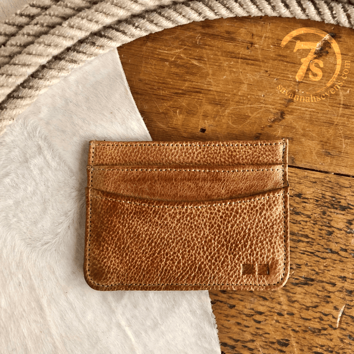 The Tilden Wallet by Savannah Sevens western life{&}style sits on a wooden surface beside a coiled rope and white textured fabric. The Savannah Sevens logo appears in the upper right corner.