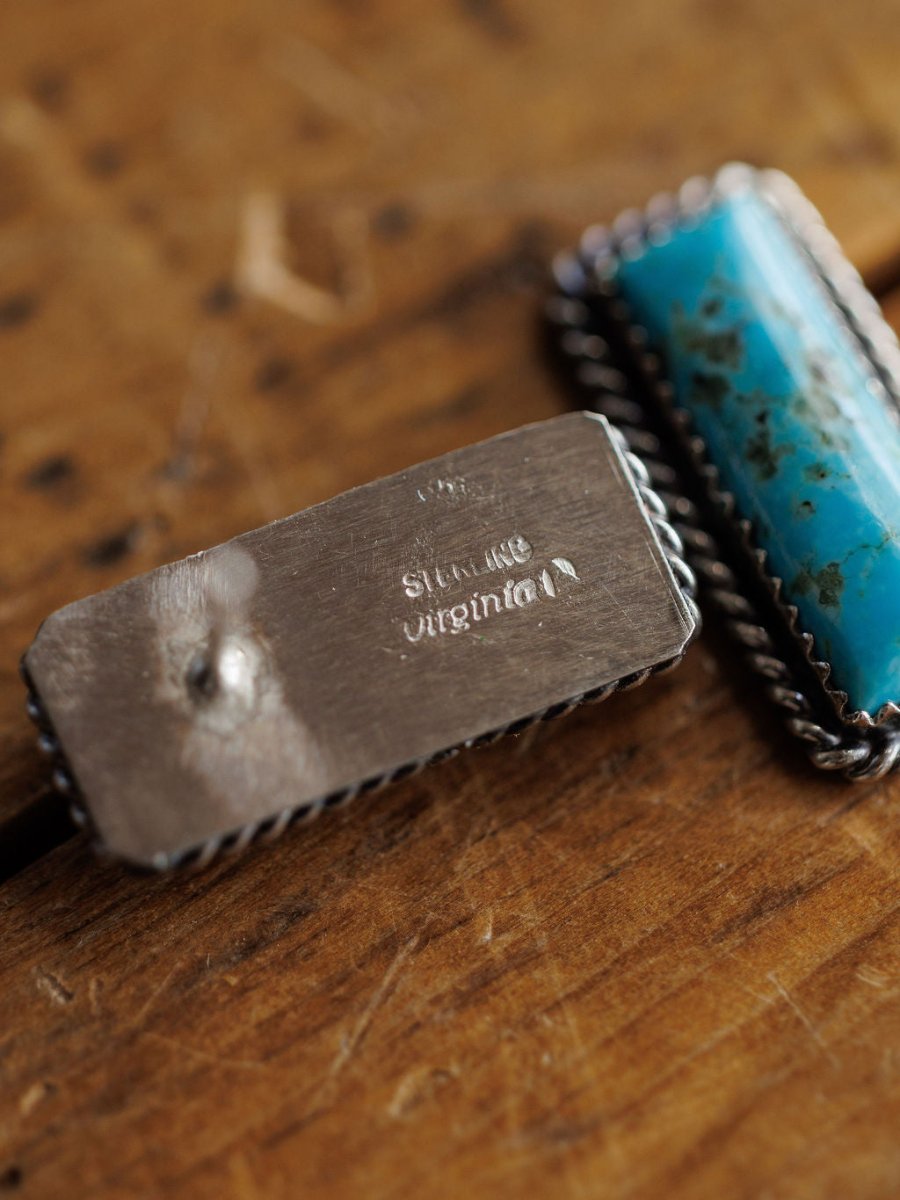 A close-up of Toano Earrings by Savannah Sevens western life{&}style and Navajo handcrafted earrings with a blue-green stone, both resting on a wooden surface.