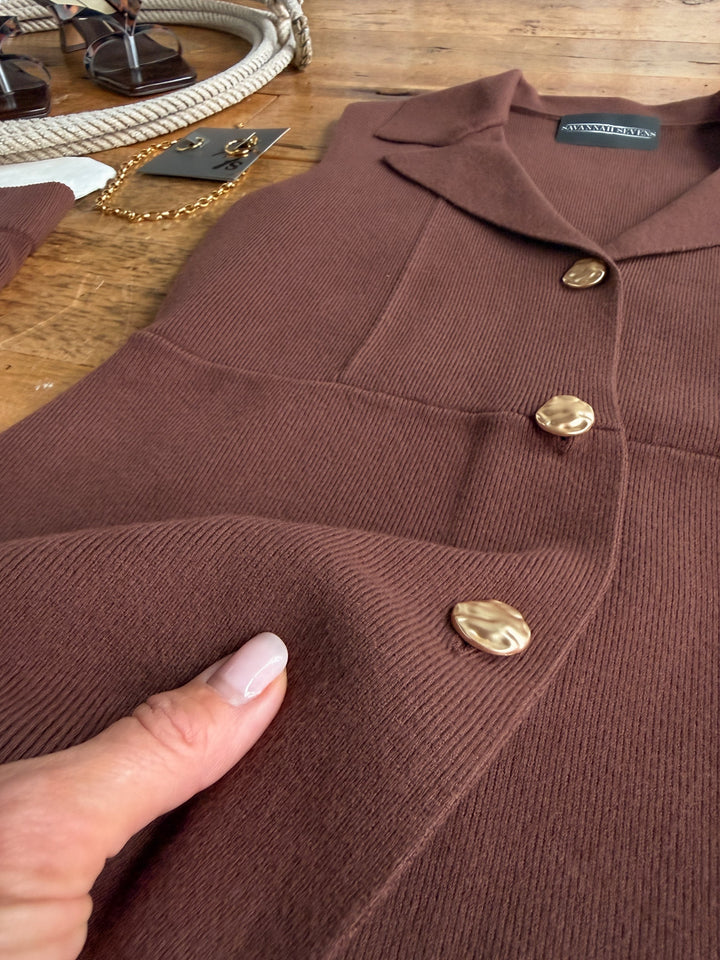 A person holds the ribbed tri-blend fabric of the Tolleson Chocolate Knit Vest Set by Savannah Sevens western life&style, highlighting its texture and detail. Accessories, such as a gold chain and sunglasses, are partially visible on a wooden table.
