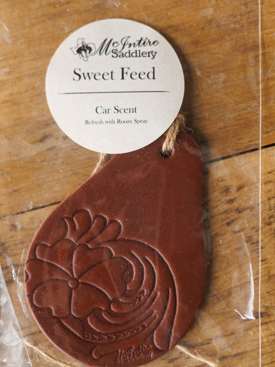 A brown, teardrop-shaped tooled leather car freshener by Savannah Sevens western life{&}style, featuring floral embossing and available in 7 scents, sits on a wooden surface in clear packaging.