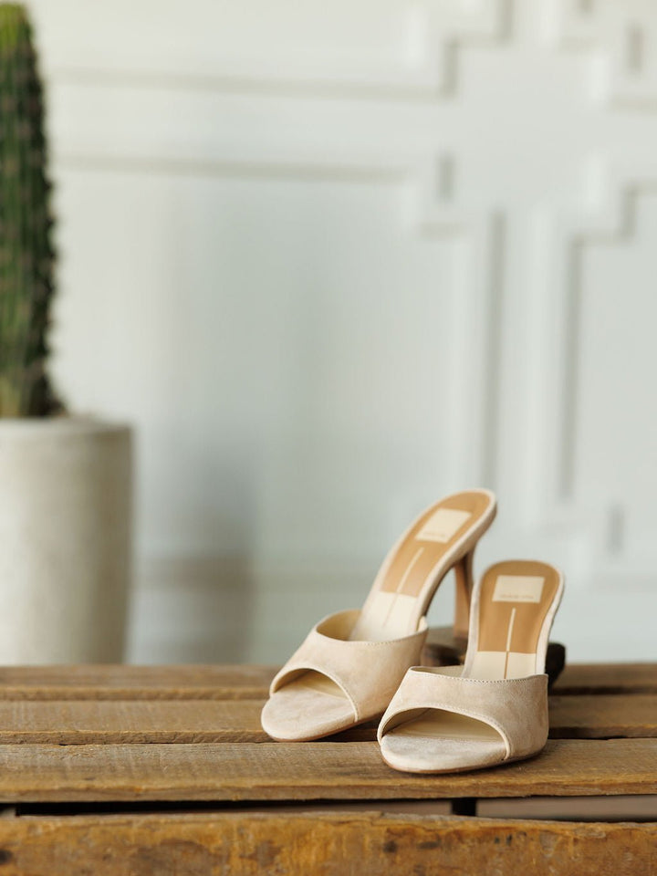 The Tulare by Savannah Sevens western life{&}style: beige suede peep toe heel sandals with a cushioned footbed and 3 3/4" heel, displayed on rustic wood with a blurred cactus and white textured wall in the background.