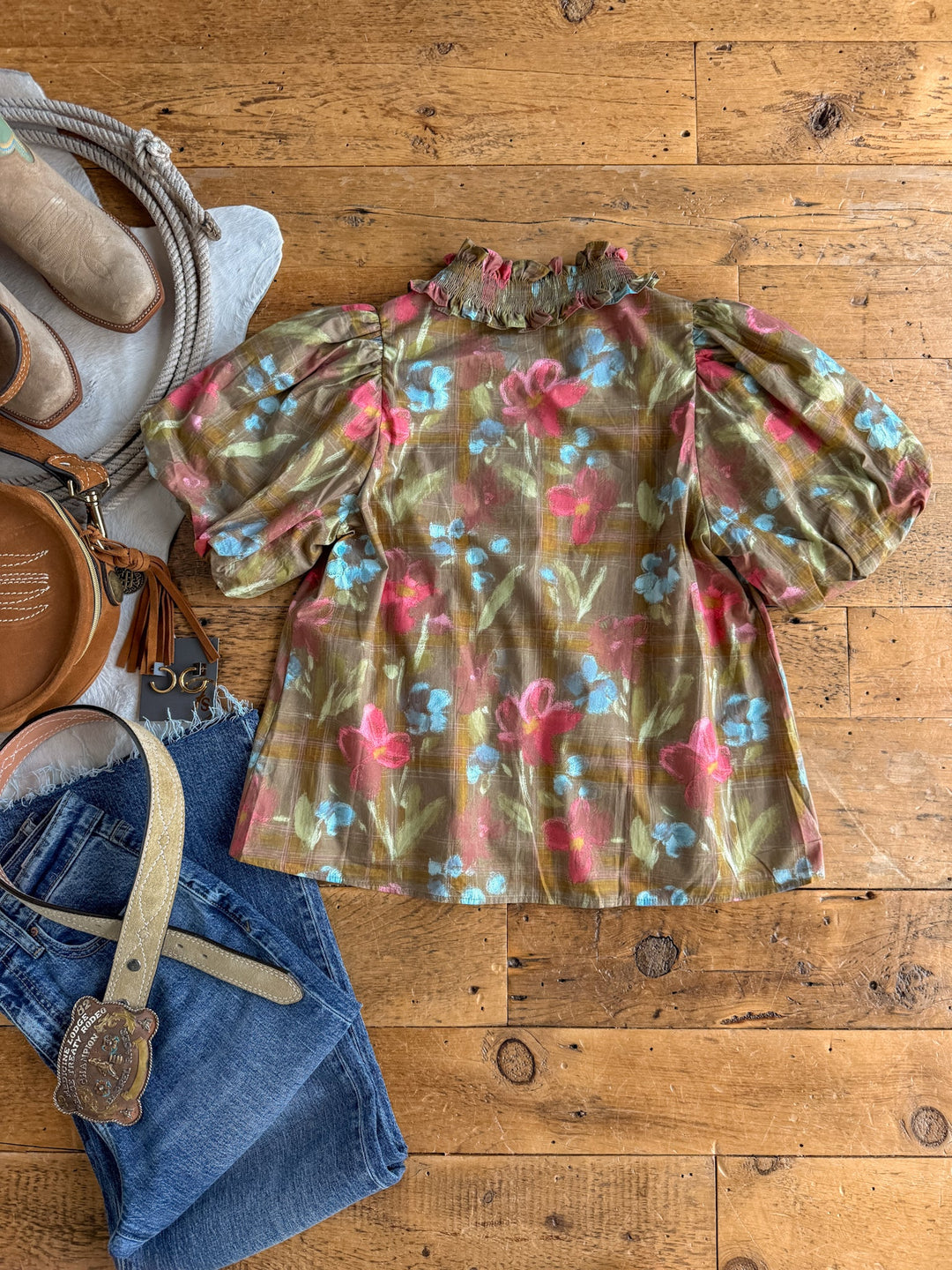 The Tupelo Olive Puff Sleeve Top by Savannah Sevens western life{&}style is displayed on a wooden floor, surrounded by blue jeans with a belt, a brown round purse, beige boots, and a gray scarf.