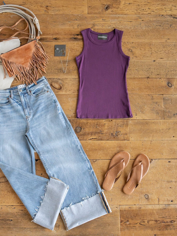 A flat lay of casual clothes: light blue cuffed jeans, the Utica Plum Ribbed Basic Tank by Savannah Sevens western life{&}style, brown sandals, a fringed purse, hoop earrings, and a necklace on a wooden floor.