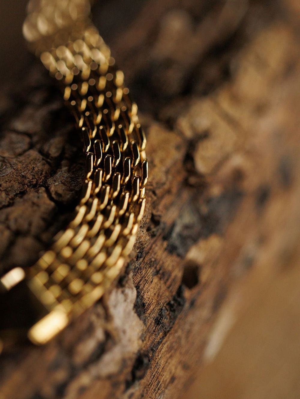 A close-up of the Vienna Bracelet by Savannah Sevens western life{&}style, an 18K gold filled, hypoallergenic watch band resting on textured wood, with a softly blurred background.