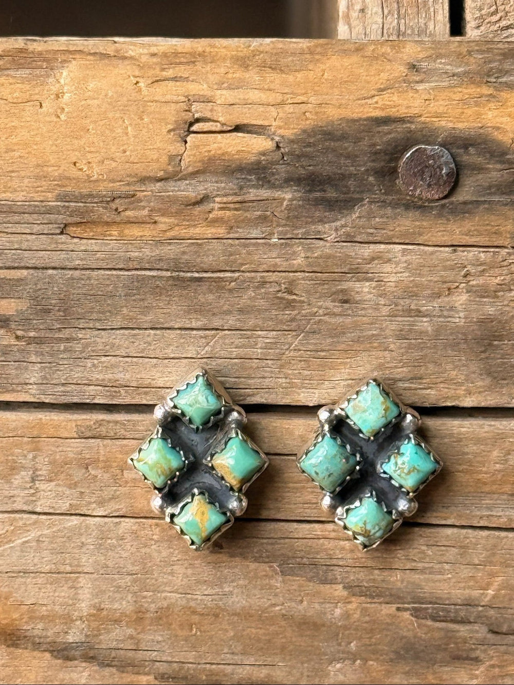 Two vintage turquoise earrings with four small Kingman turquoise stones set in a diamond shape, displayed on a rustic wooden surface with visible grain and a nail.