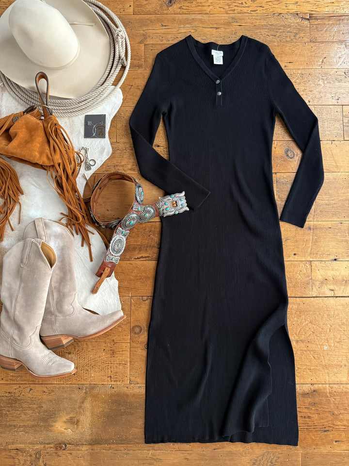 The Walhalla Black Ribbed Dress by Savannah Sevens western life{&}style is styled on a wooden floor with a white hat, brown fringe bag, turquoise belt, silver jewelry, white cowboy boots, and jeans.