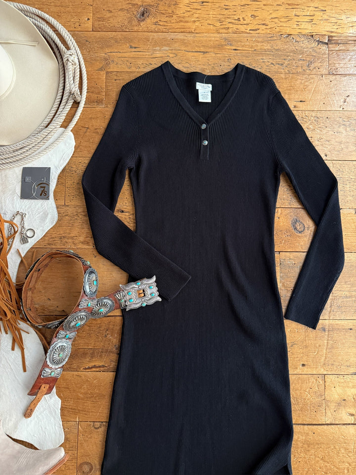 The Walhalla Black Ribbed Dress by Savannah Sevens western life{&}style is laid flat on a wooden floor, paired with a tan hat, fringed brown bag, multicolored embroidered belt, and jewelry for a versatile, stylish look.