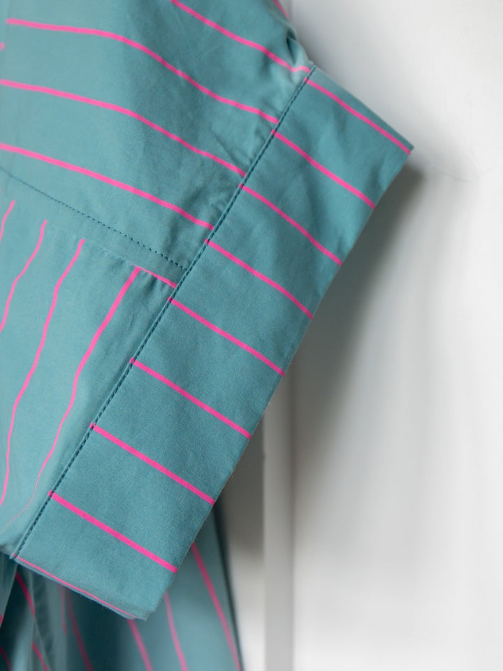 A close-up of the Wapello Turquoise Blue Button Up Top by Savannah Sevens western life{&}style shows detailed stitching and a folded sleeve with vertical and horizontal stripes on a light background.