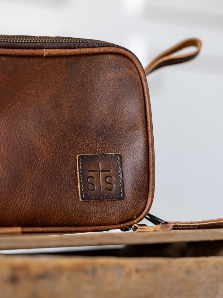 Close-up of the Wayneboro Leather Shave Bag by Savannah Sevens western life{&}style, featuring a stitched logo. The blurred background highlights the rich leather texture and quality craftsmanship of this stylish dopp kit.