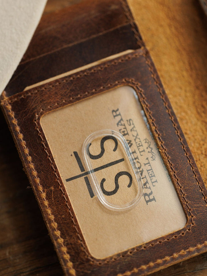 A close-up of the Waynesboro Leather Money Clip Wallet by Savannah Sevens western life{&}style, crafted from full grain leather with visible stitching, a worn texture, and a transparent ID slot displaying a S/S RANCHWEAR TELL TEXAS card.