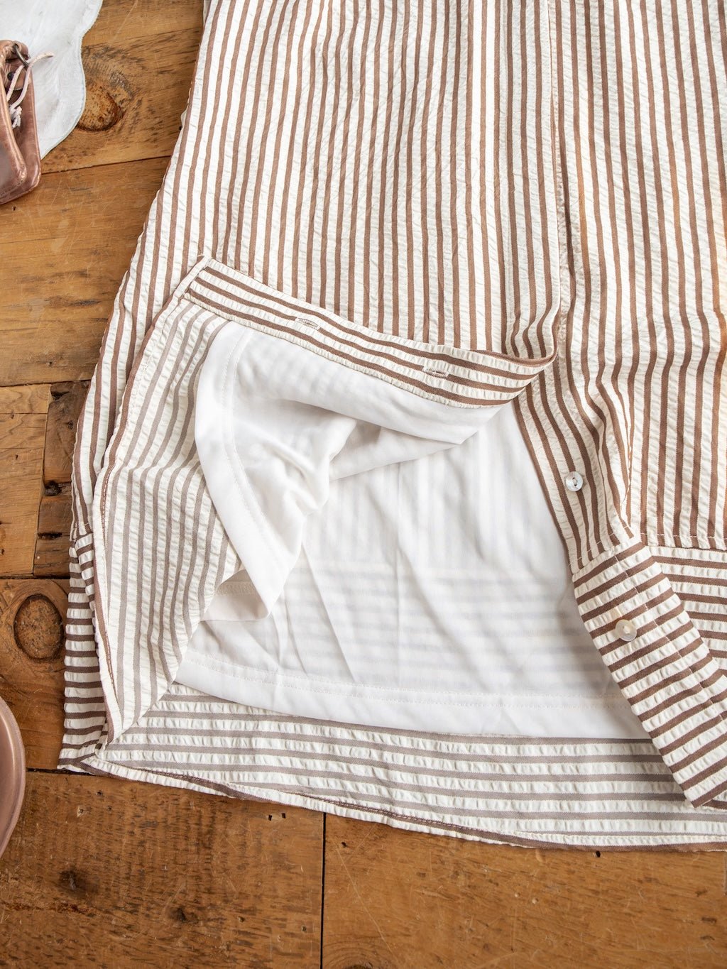 The Westerly Brown Striped Button Up Dress by Savannah Sevens western life{&}style is displayed on a wooden surface, with the lining partially turned out to reveal the inside fabric and seam details.