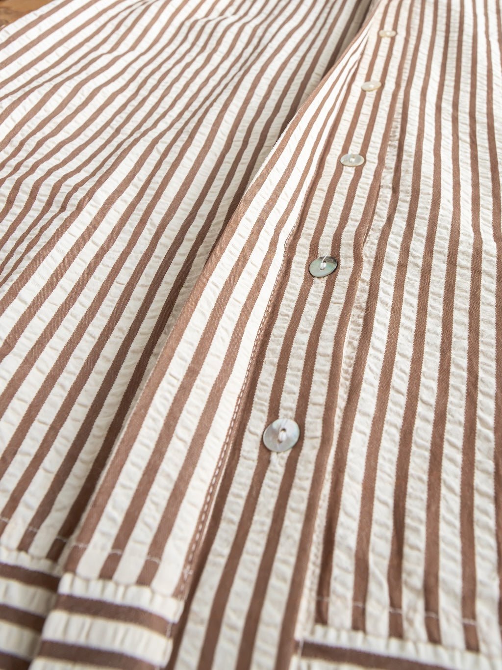 Close-up of the Westerly Brown Striped Button Up Dress by Savannah Sevens western life{&}style, featuring brown and cream stripes, pearl-like buttons, and a textured fabric. The dress is laid flat to showcase its button details and bold stripes.
