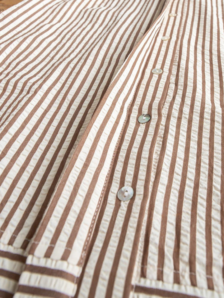 Close-up of the Westerly Brown Striped Button Up Dress by Savannah Sevens western life{&}style, featuring brown and cream stripes, pearl-like buttons, and a textured fabric. The dress is laid flat to showcase its button details and bold stripes.