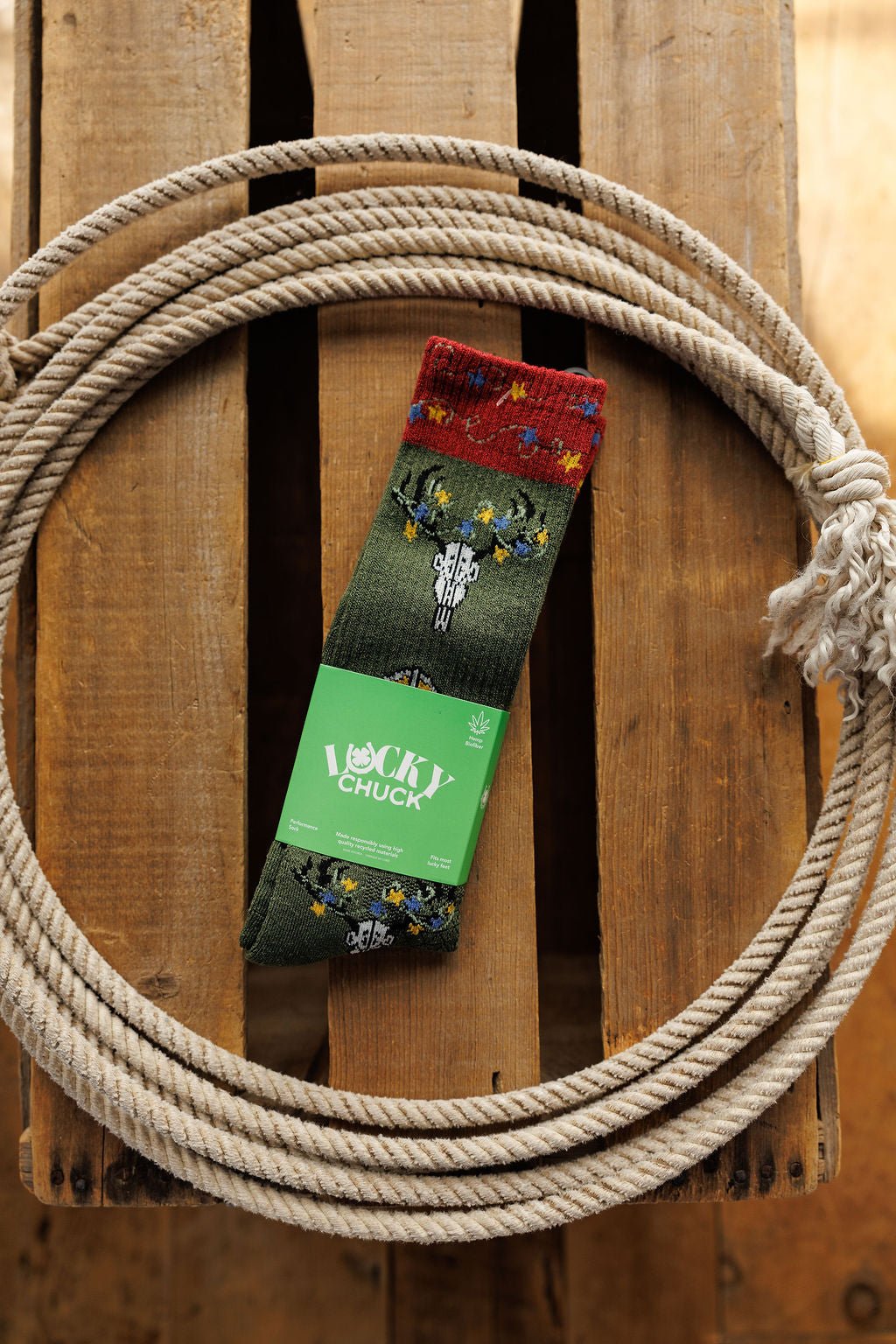 A pair of Western Lights Crew Socks by Savannah Sevens western life{&}style, featuring a green cactus and flower pattern, rests inside a coiled rope on wood. These lightweight, breathable socks are designed for Western performance.