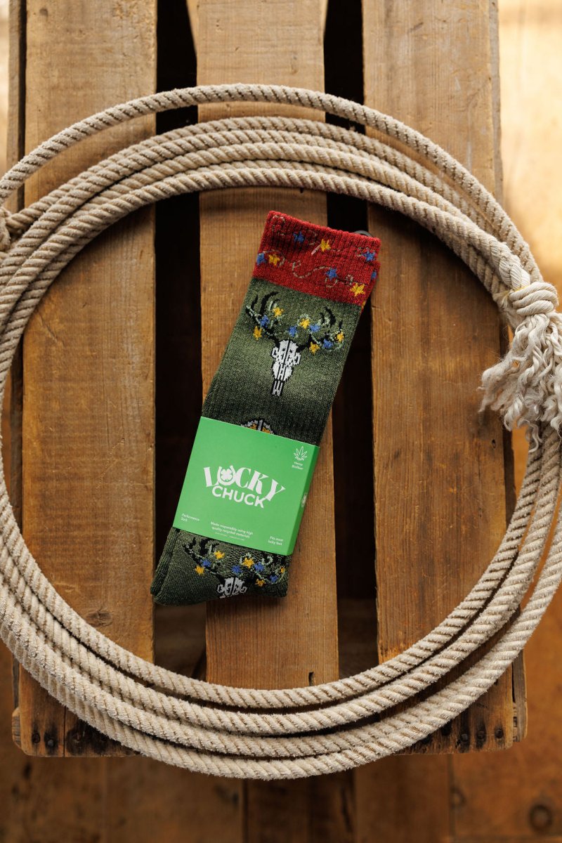 A pair of Western Lights Crew Socks by Savannah Sevens western life{&}style, featuring a green cactus and flower pattern, rests inside a coiled rope on wood. These lightweight, breathable socks are designed for Western performance.