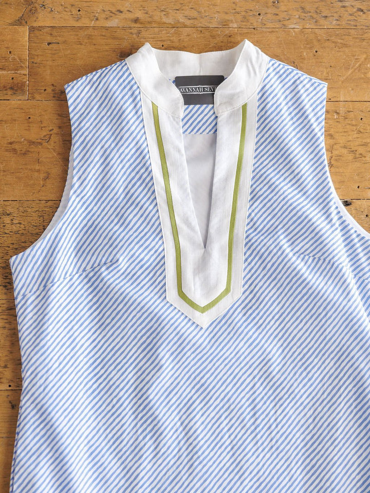 The Westland Blue Pinstripe Cotton Dress by Savannah Sevens western life{&}style features light blue and white stripes, a sleeveless design with a white V-neck trimmed in olive green, and is shown flat on wood. Contemporary sizing offers a flattering fit.