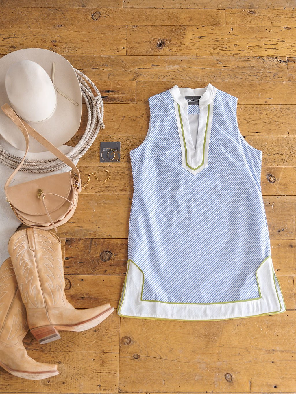 The Westland Blue Pinstripe Cotton Dress by Savannah Sevens western life{&}style is displayed on a wooden floor with tan cowboy boots, a beige wide-brim hat, a tan crossbody bag, and a metallic bracelet. Contemporary sizing available.