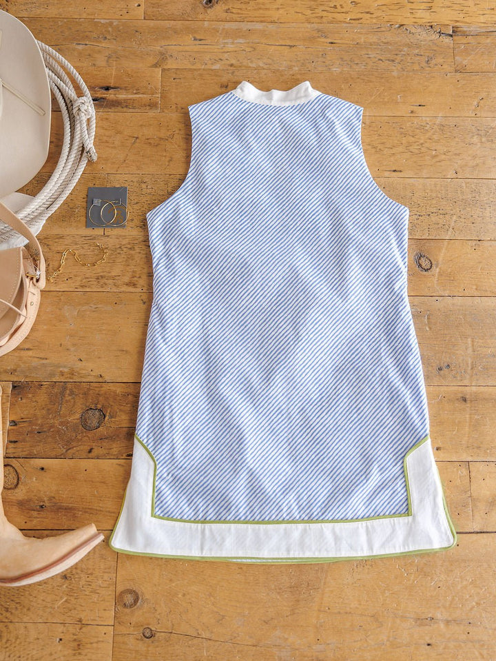 The Westland Blue Pinstripe Cotton Dress by Savannah Sevens western life{&}style features green trim and a sleeveless cotton design, laid flat with a tan hat, sandals, and a small square item. Contemporary sizing offers a flattering fit.
