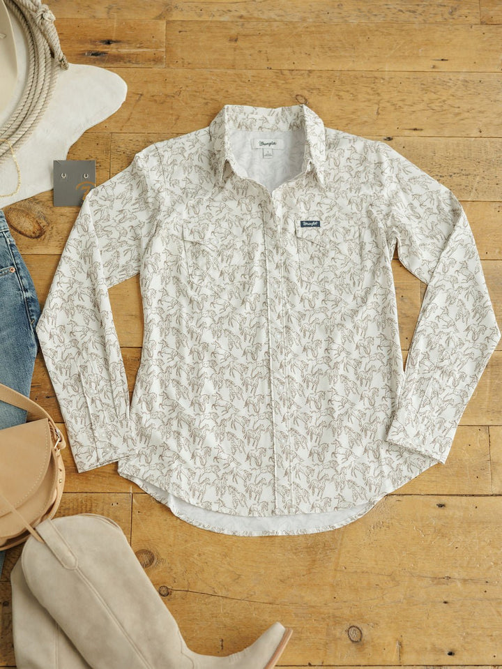 The Weston Wrangler Horse Button Top by Savannah Sevens western life{&}style, a white long-sleeve women’s shirt with a subtle leaf print, is styled with tan boots, a tan handbag, light blue jeans, a hat, and earrings on a wooden floor.