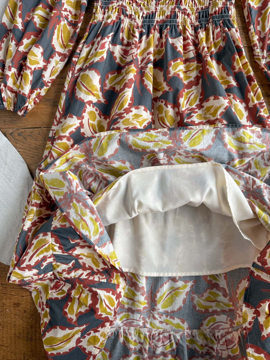 The Westphalia Floral Dress by Savannah Sevens western life{&}style is turned inside out on a wooden surface, revealing the lining and stitching details along its cotton long sleeves and shirred waist.
