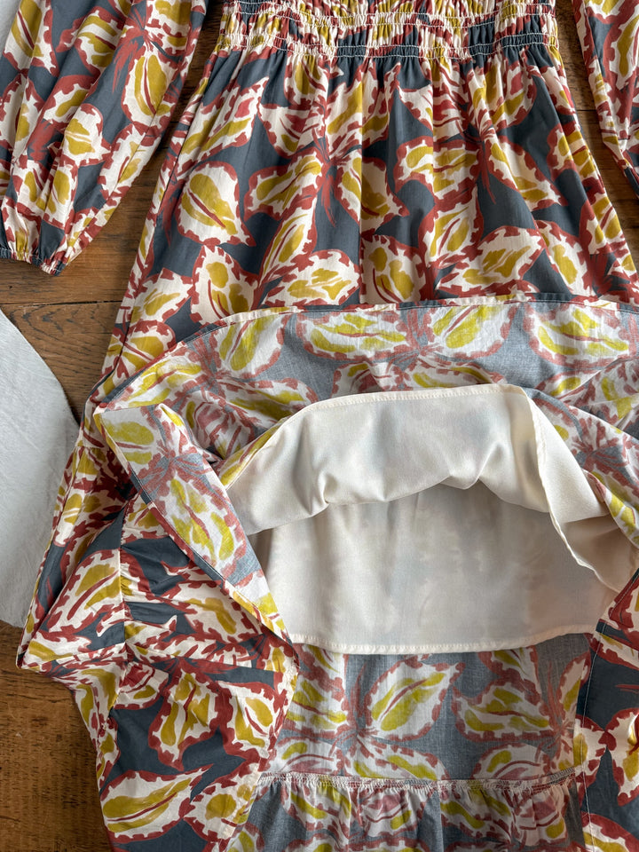 The Westphalia Floral Dress by Savannah Sevens western life{&}style is turned inside out on a wooden surface, revealing the lining and stitching details along its cotton long sleeves and shirred waist.