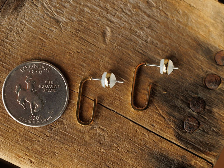 A Wyoming state quarter sits beside the Savannah Sevens western life{&}style Westport Earrings—18K gold plated geometric design with pearl accents—on a rustic wood surface with metal studs.