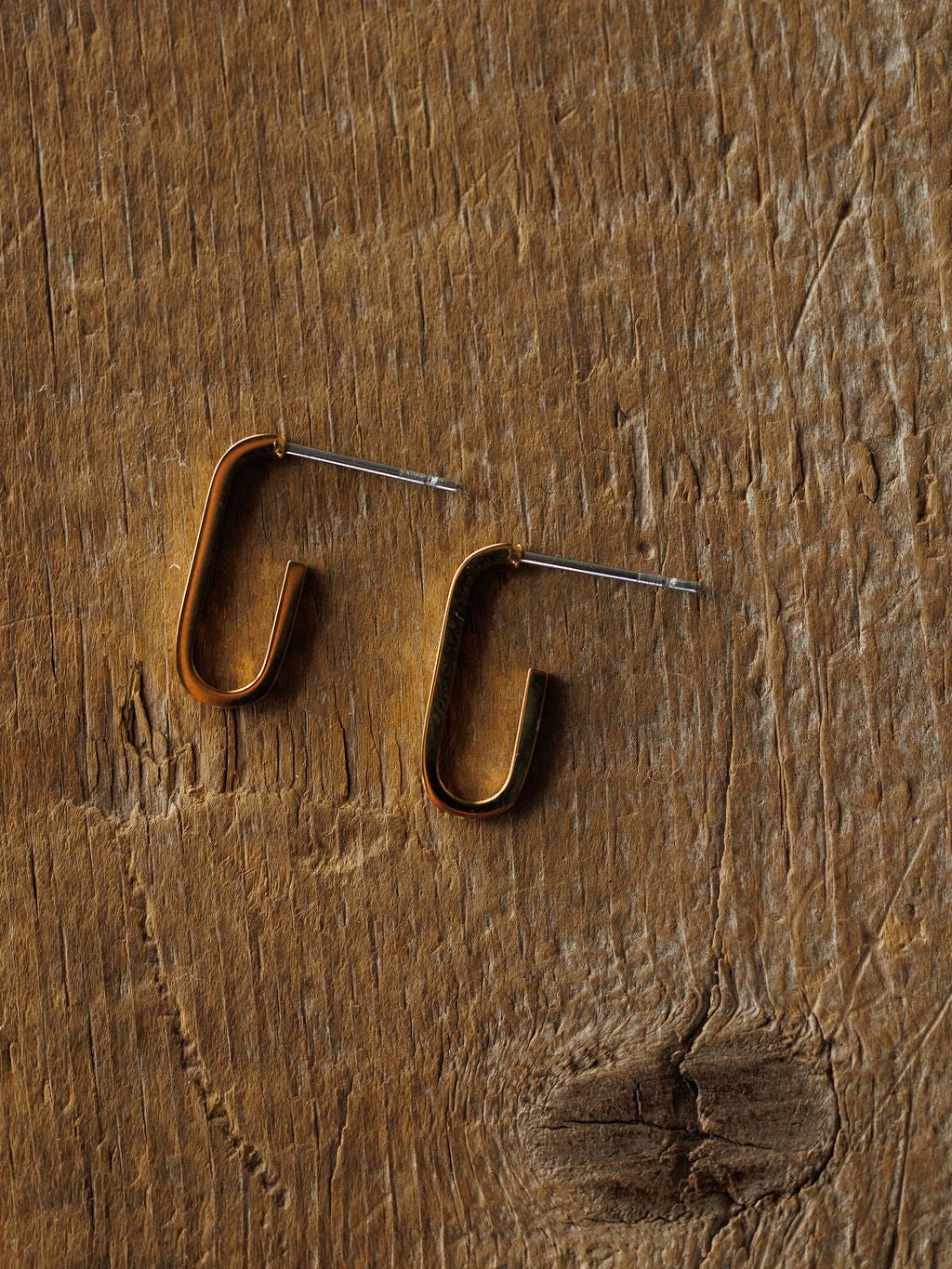 The Westport Earrings by Savannah Sevens western life{&}style are minimalist 18K gold plated rectangular hoop earrings with straight posts, shown on a textured wooden surface.